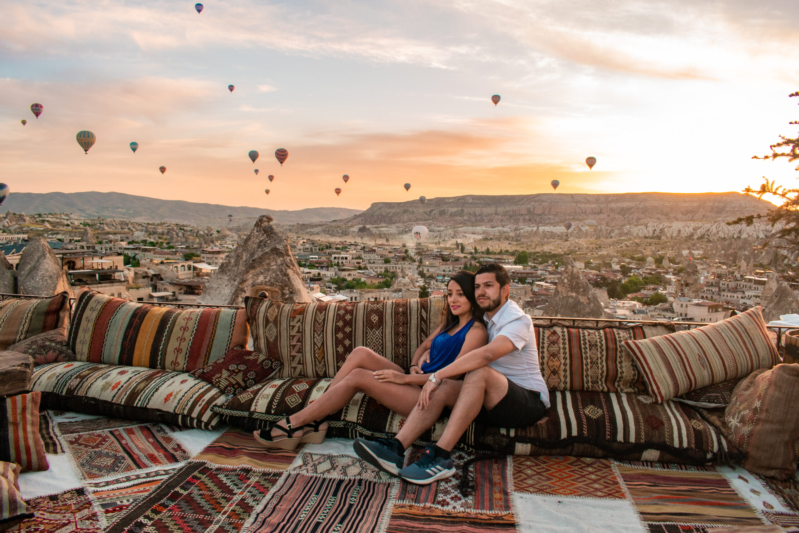 Pareja viajera explorando Capadocia con globos de fondo Pareja disfrutando de la mágica vista de Capadocia, con sus formaciones rocosas únicas y globos aerostáticos flotando en el cielo al amanecer