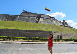 Viajera disfrutando de un recorrido por Cartagena, Colombia, con el majestuoso Castillo San Felipe de Barajas al fondo, símbolo histórico de la ciudad y su patrimonio colonial