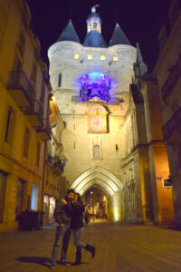 Pareja viajera explorando Burdeos, Francia, frente a una de sus puertas históricas medievales, símbolo del pasado arquitectónico y cultural de la ciudad.