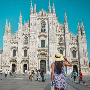 Mujer viajera de espaldas, contemplando la majestuosa Catedral de Milán, Italia, uno de los ejemplos más impresionantes de arquitectura gótica en Europa.